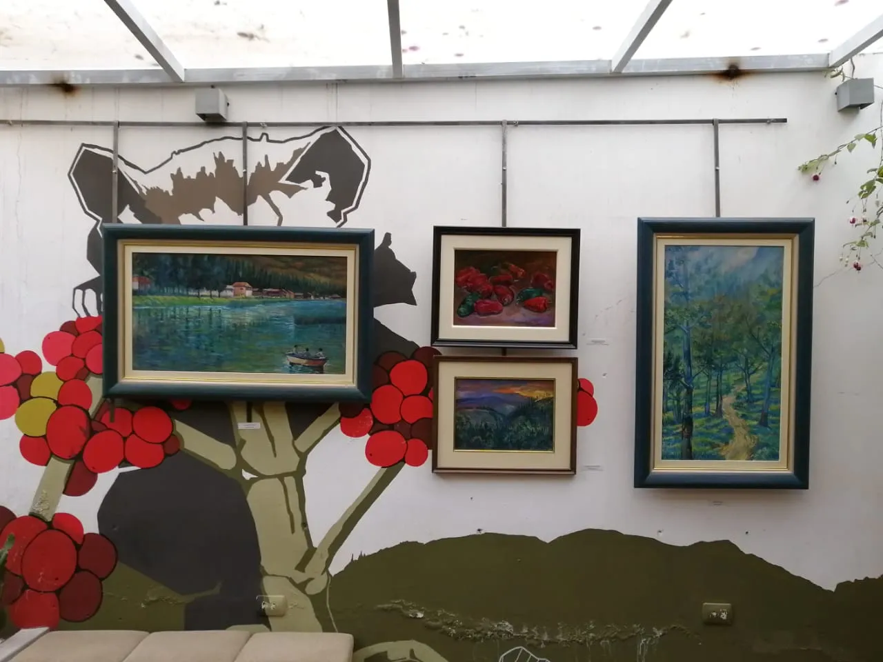Cuatro cuadros colgados sobre un mural con ramas y flores rojas