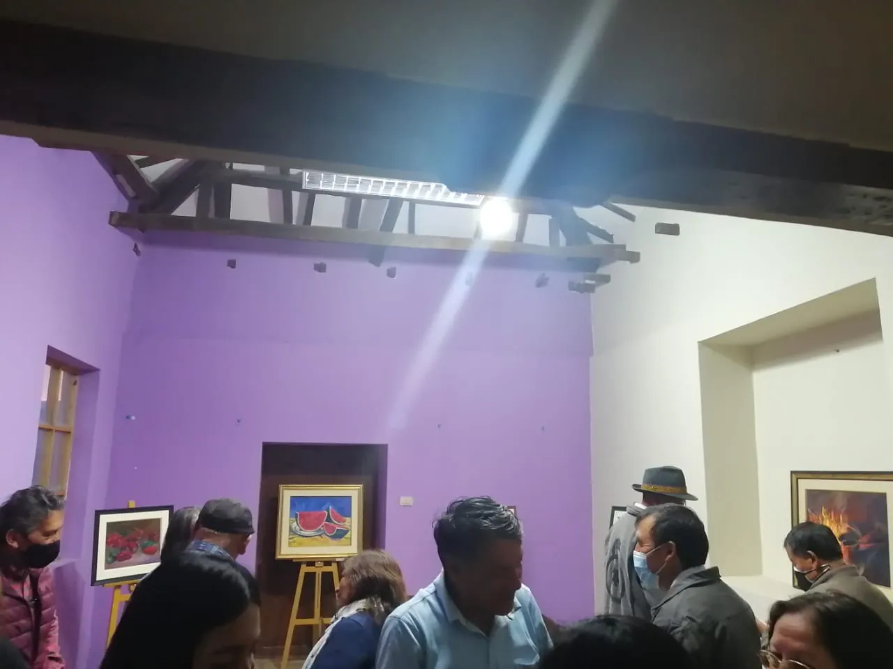 Visitantes en la sala de techo de madera, con los cuadros sobre caballetes