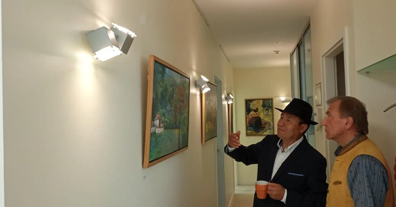 Alejandro Galindo explica un cuadro a un visitante en el pasillo de la sala