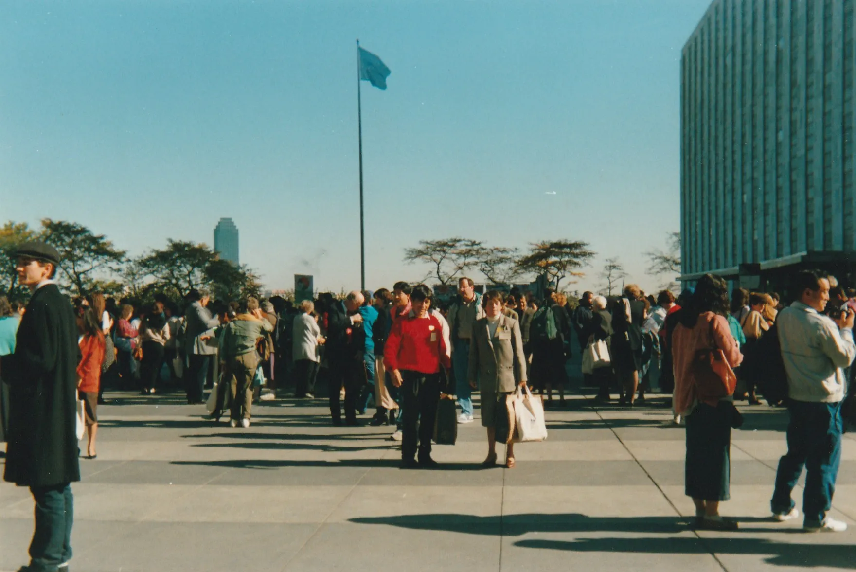 Alejandro Galindo, con jersey rojo y bolsas en las manos, en la plaza de la sede de las Naciones Unidas, con la bandera azul de la ONU al fondo