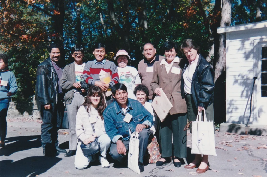 Foto de grupo de la delegación al aire libre, entre árboles en otoño; Alejandro Galindo, de pie, con jersey gris y rojo a rayas y un libro en las manos