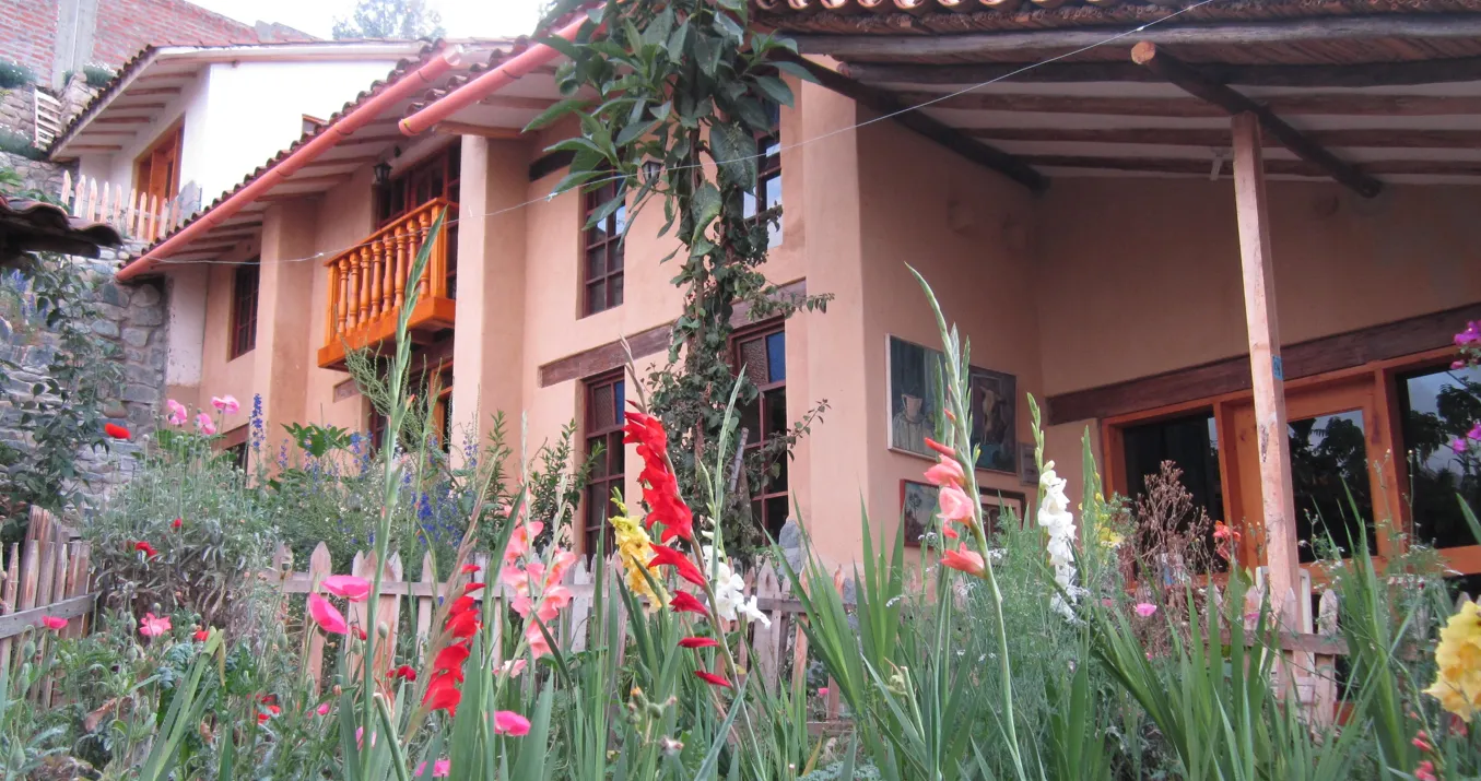 Casa de dos plantas con balcón de madera, paredes de tierra de color y jardín