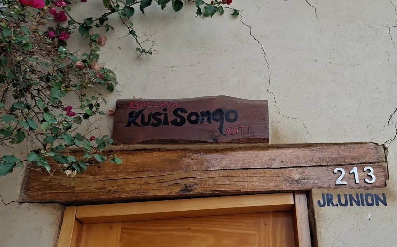 Rótulo de madera «Galería Kusi Sonqo Arte» sobre la puerta de la casa, en el jirón Unión 213, con una buganvilla encima