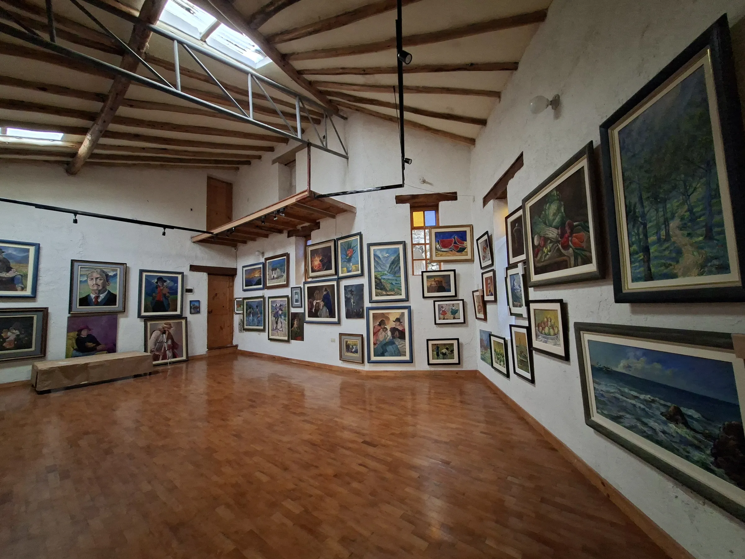 Sala de la galería, con techo de vigas de madera y lucernarios, suelo de parqué y las paredes llenas de cuadros