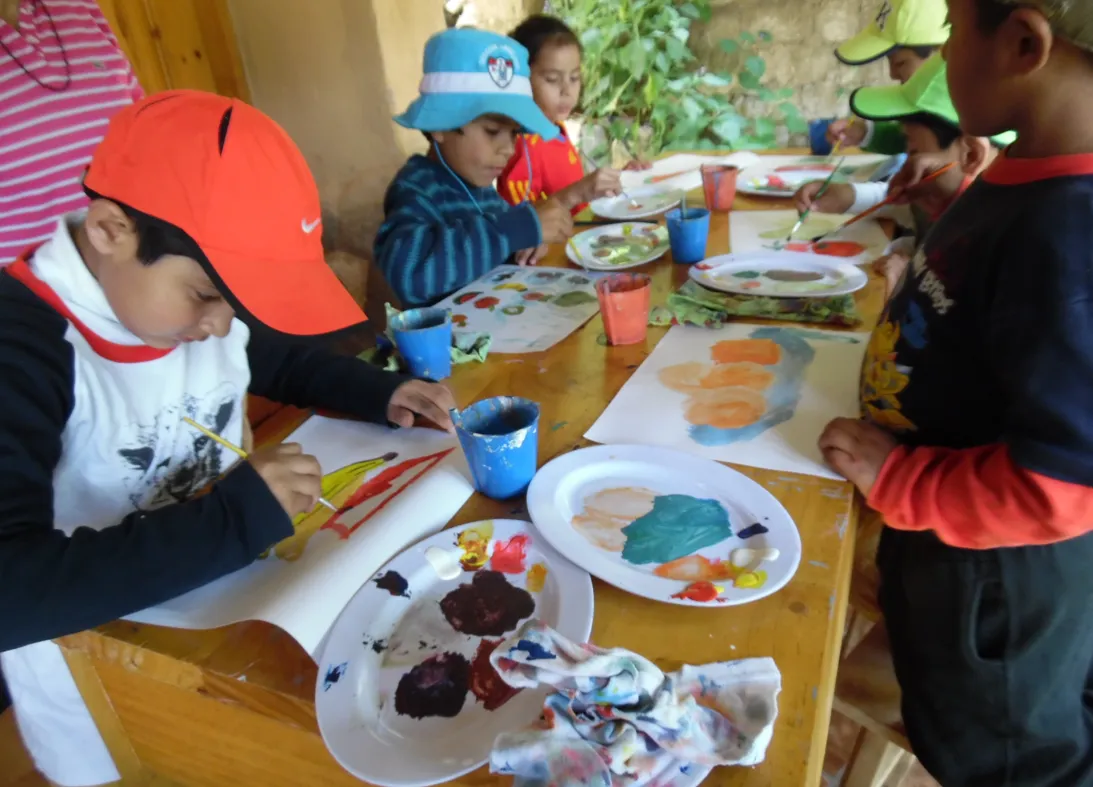 Niños con gorras pintan con témperas sobre platos de plástico
